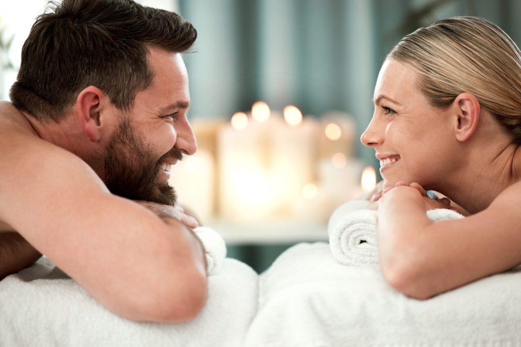 Couple face à face souriant et détendu qui se regarde, allongé sur une table de massage.