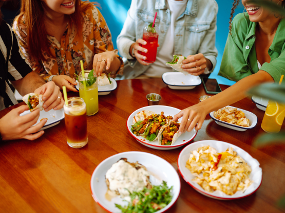 Des amis partagent un repas au restaurant, les assiettes sont sur la table, breuvages à la main